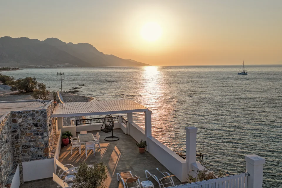 The roof terrace at sunset with sun loungers and a sailing boat on the Aegean