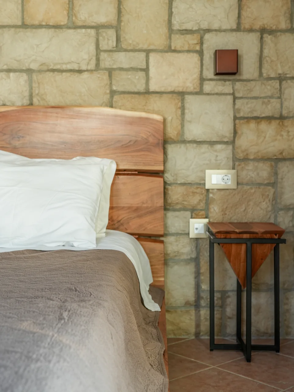Bedroom with stone wall, wooden headboard and reading lamp