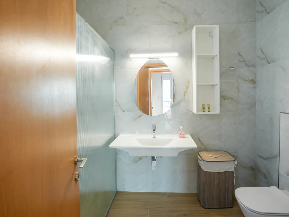 Marble bathroom with round mirror and wooden vanity